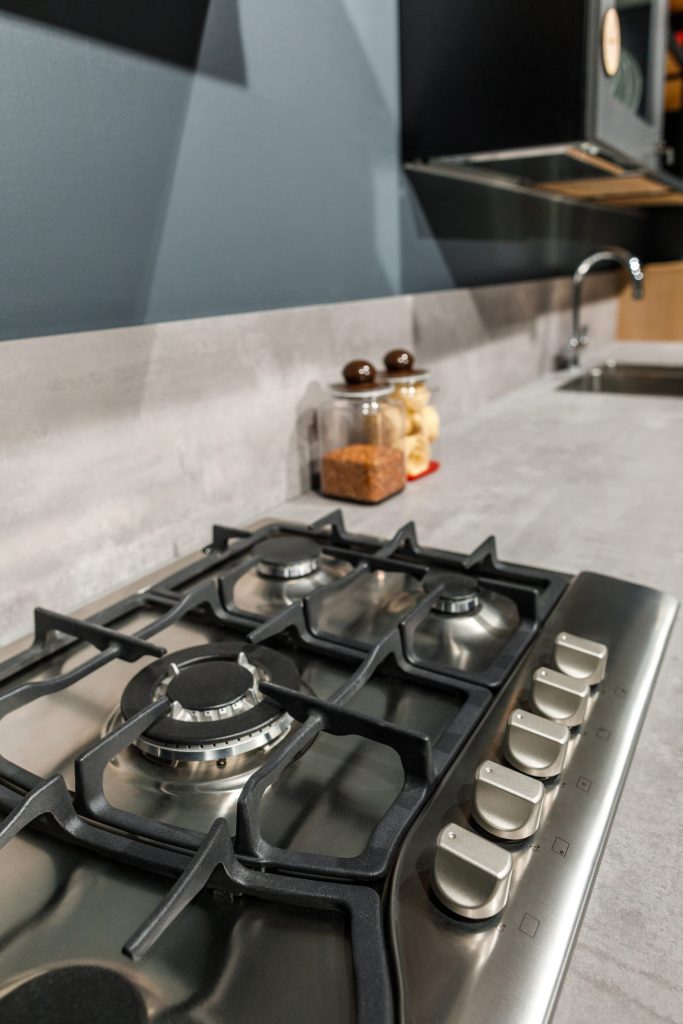 A stainless gas hob photographed close along the surface, the control knobs in a row and the burner caps and pan supports in focus