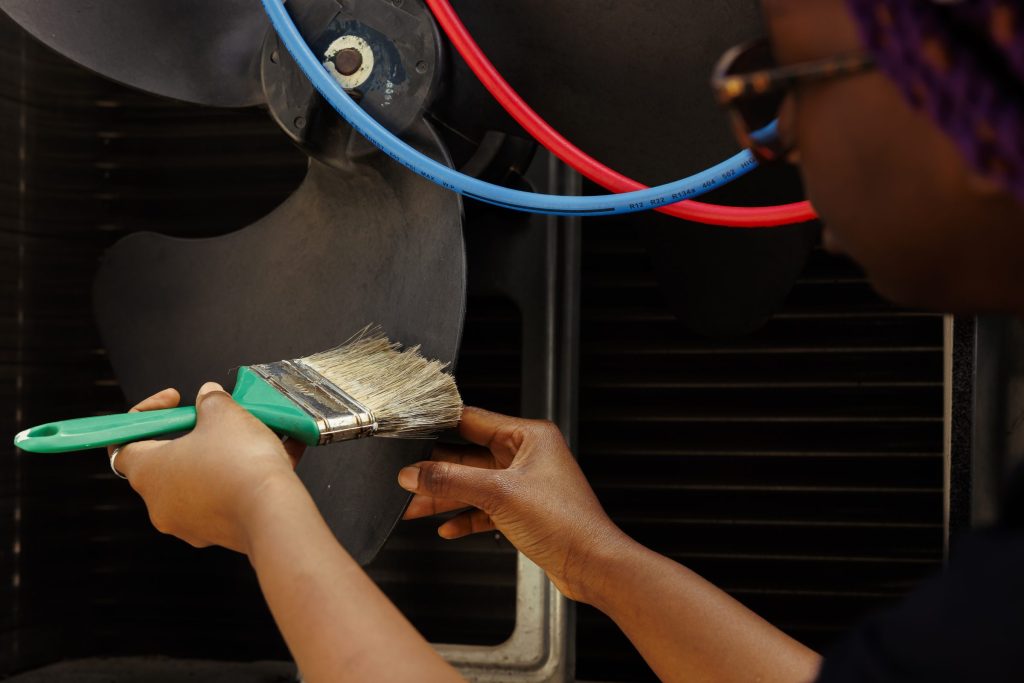 A brush working dust off a coil and fan behind an appliance.