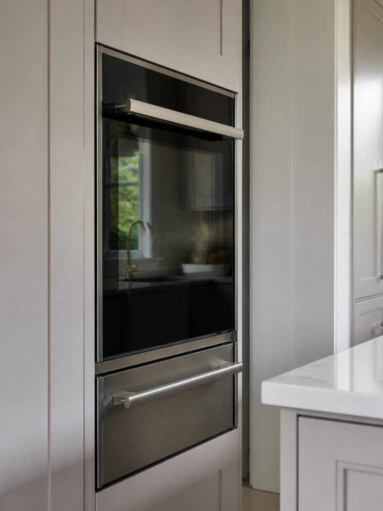 A built-in oven set into a tall cabinet column above a warming drawer, door closed on dark glass.