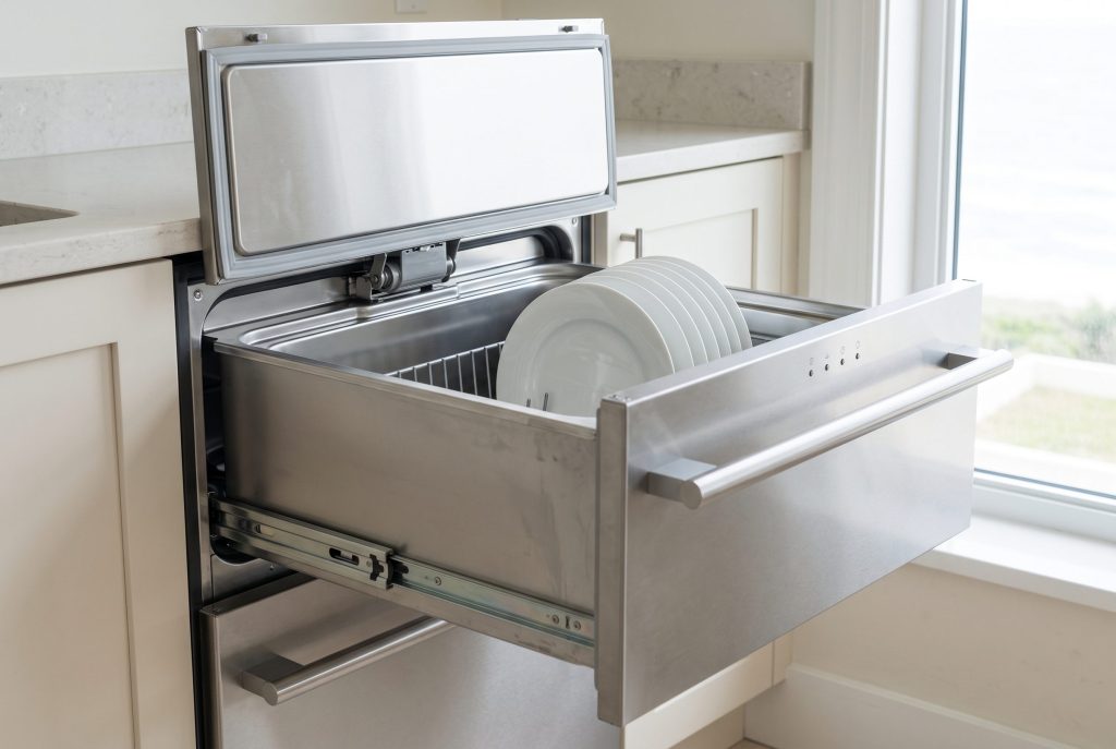 A dish drawer dishwasher open with plates in the basket, a row of small unlit indicator lamps along the top edge of the front
