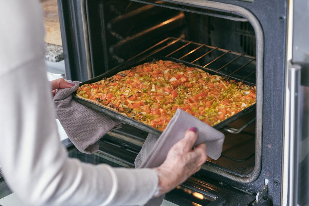 Adult baking savory pizza in oven at home.