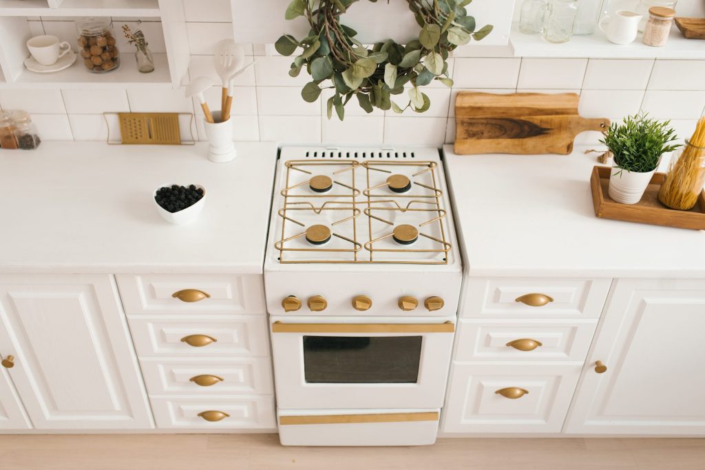 An oven in a bright kitchen with white cabinets and gold.