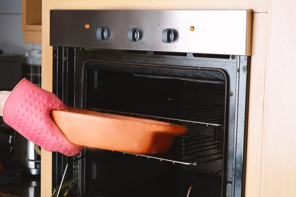 A dish being lifted out of the oven in a pink oven glove.