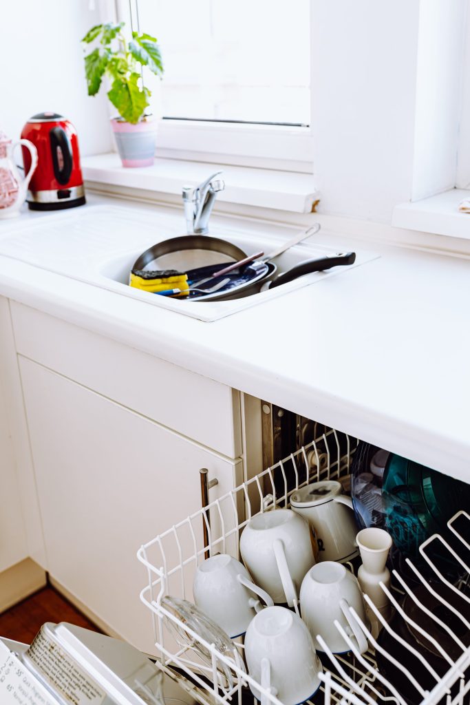 A dishwasher in a dishes and cups in kitchen sink.
