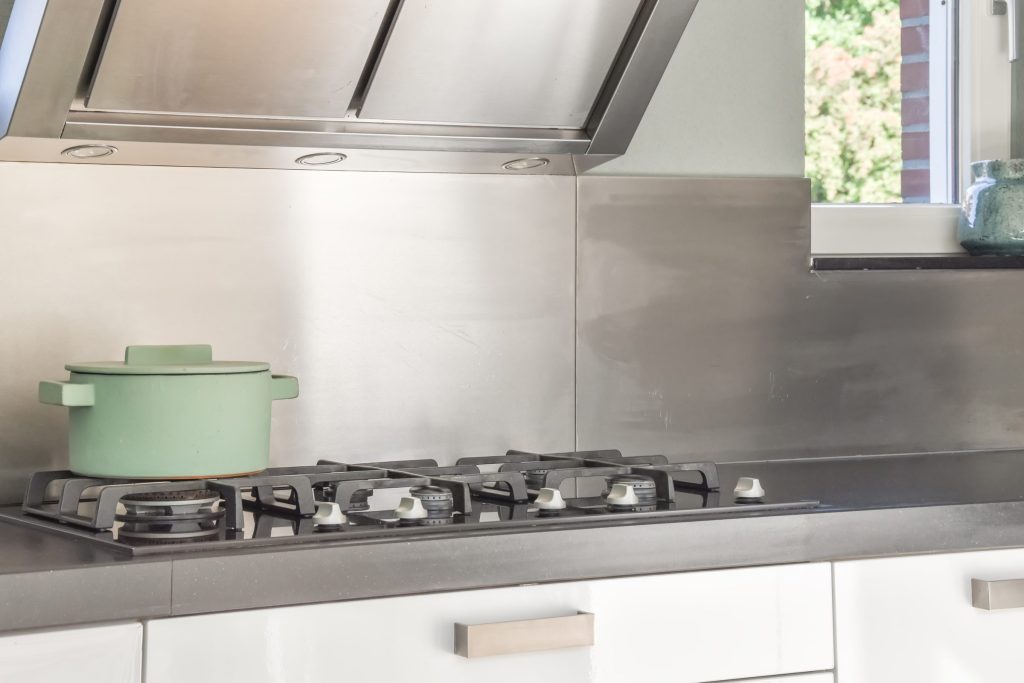 A green pot on the burner of a gas cooktop set into a stone counter.