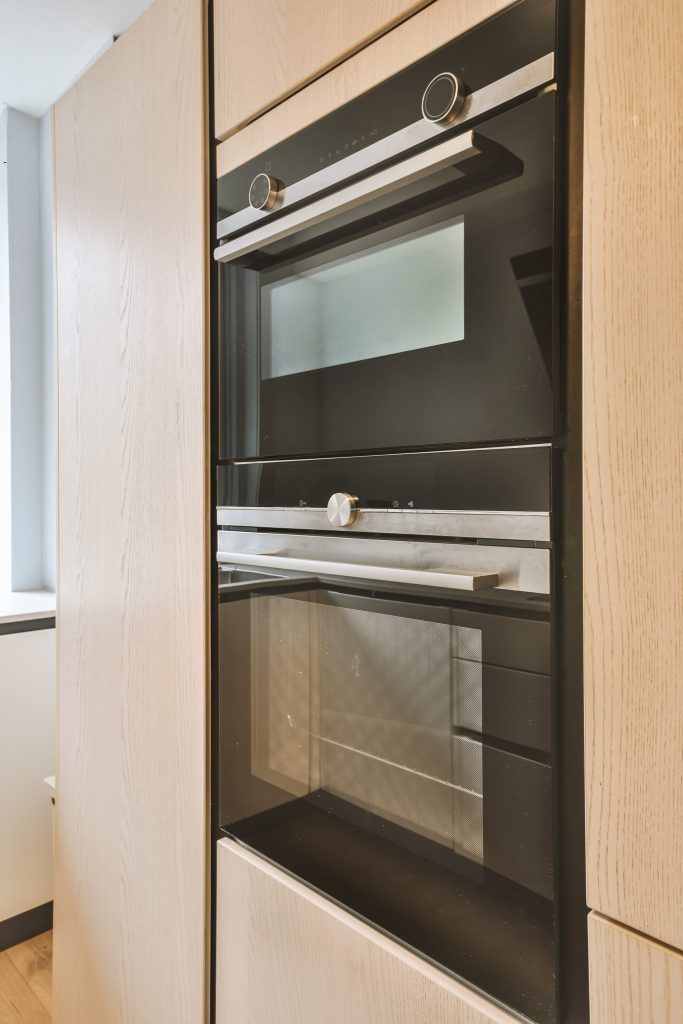 Modern oven built into wooden kitchen cabinet.