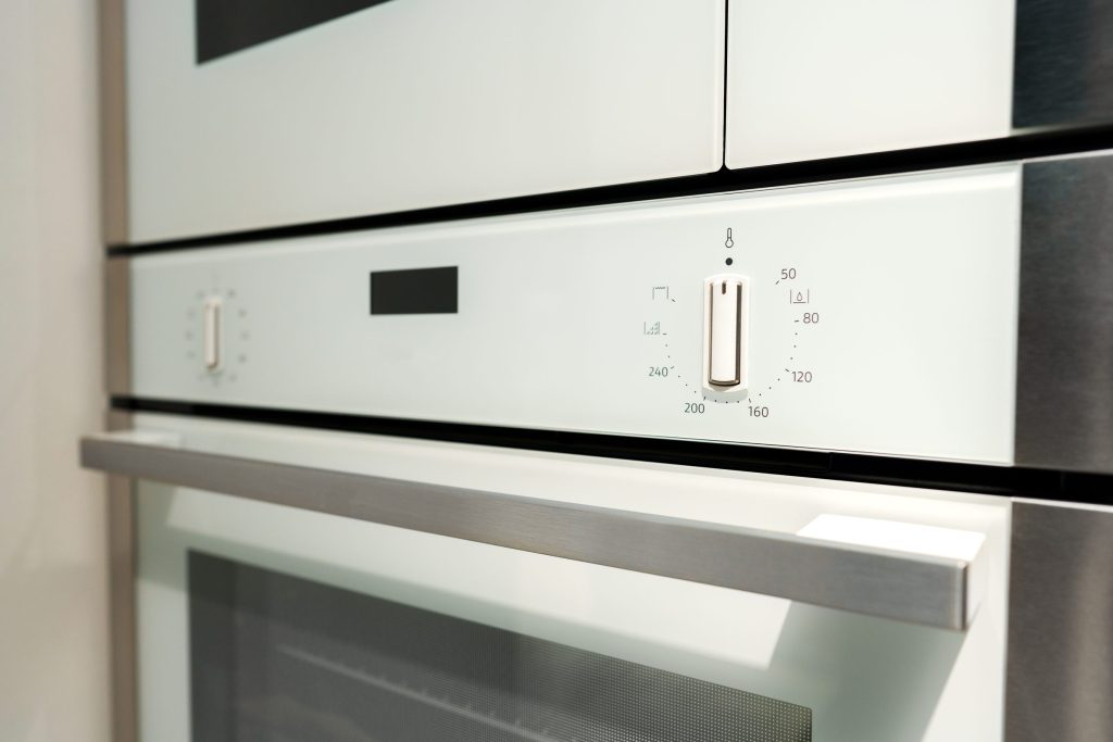 Close-up of the fascia of a white built-in oven, its temperature dial and function markings sharp against the enamel.