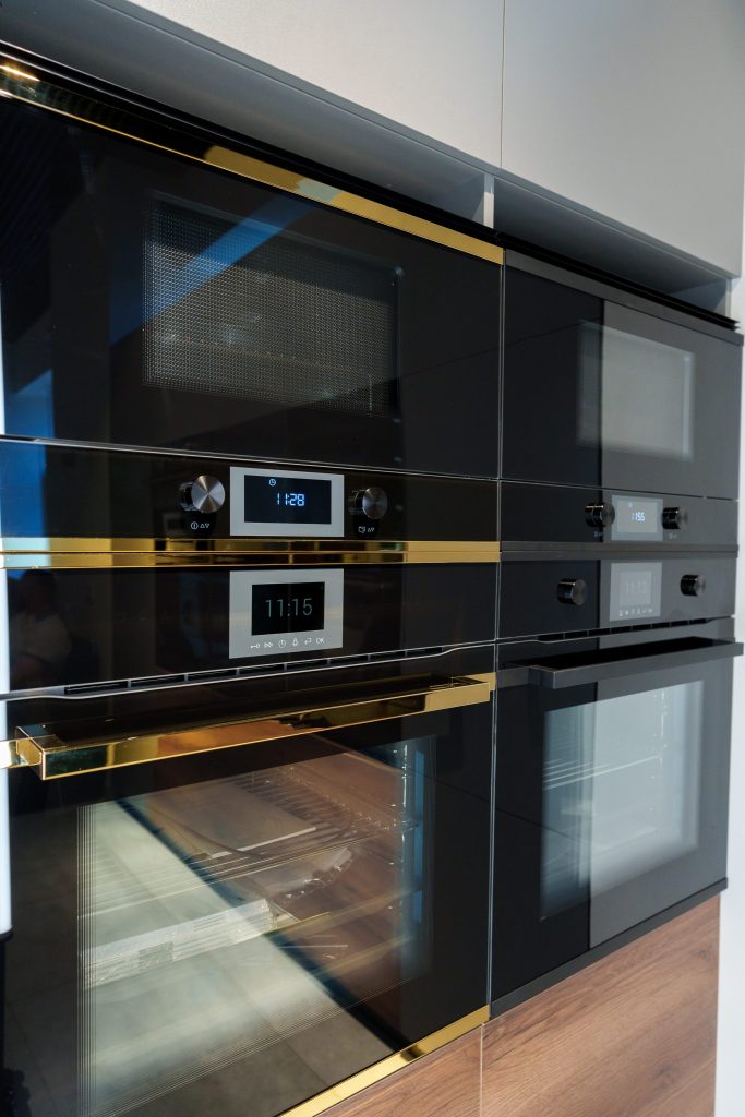 A black glass oven and combination microwave stacked in a tall run of dark cabinetry, the oven door open.