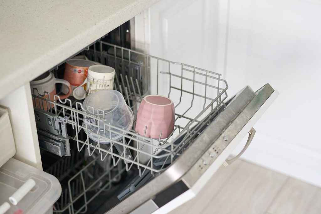 Open dishwasher filled with mugs and plastic.