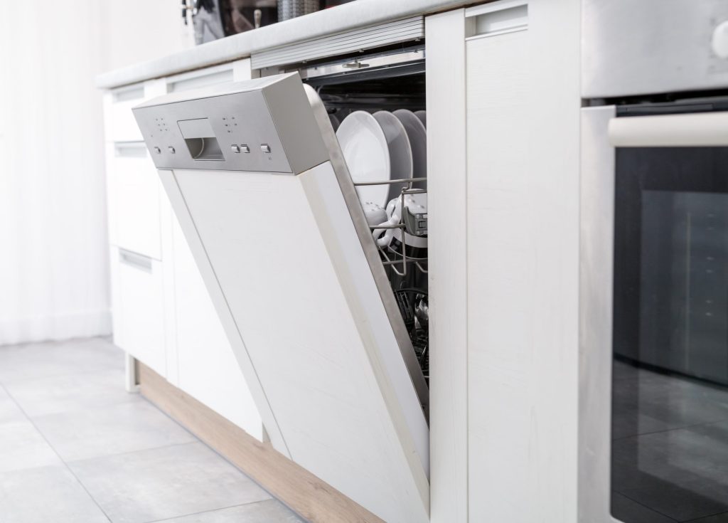 A panel-ready dishwasher standing open in a fitted kitchen, its baskets drawn out.