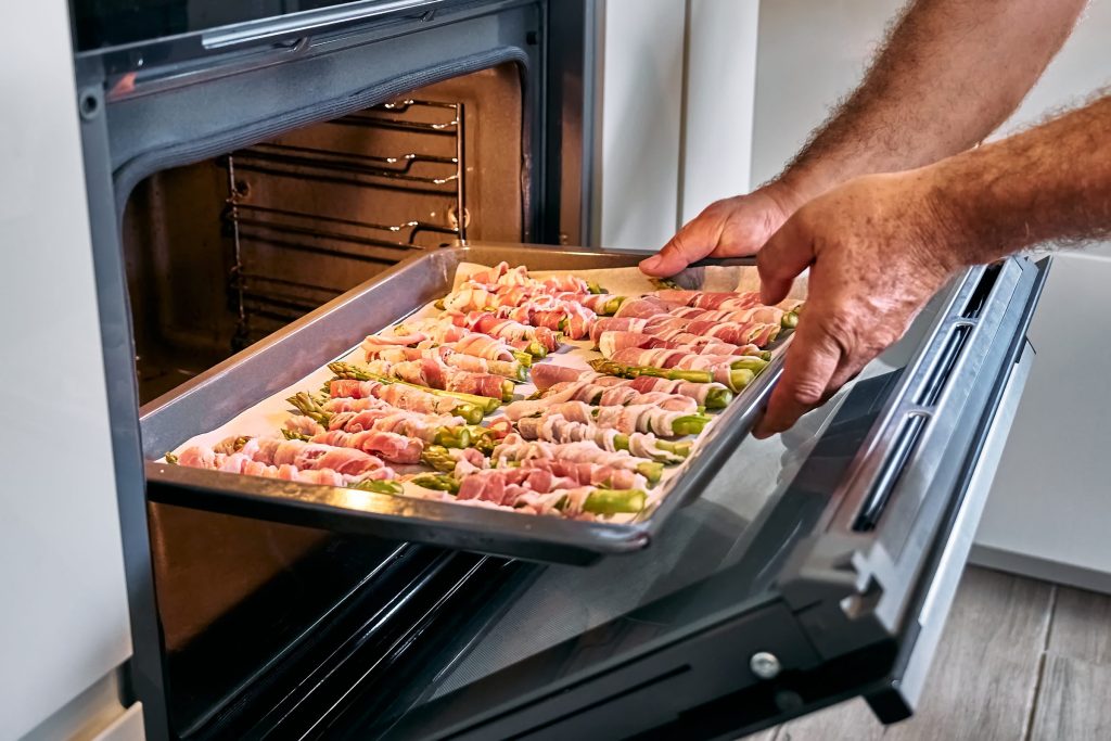 Preparing asparagus wrapped in meat in the oven.