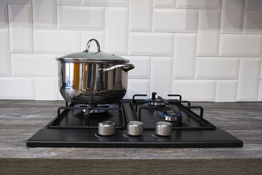 A stainless steel pot standing on the burners of a range.