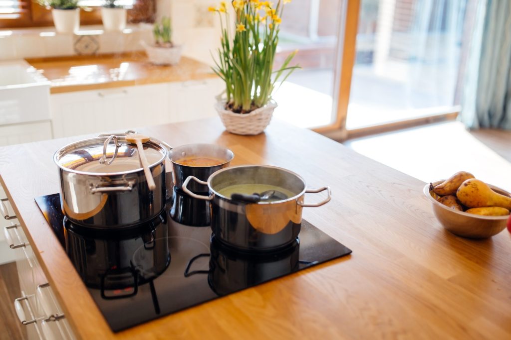 Stockpots simmering on the burners of a cooktop in a home kitchen.