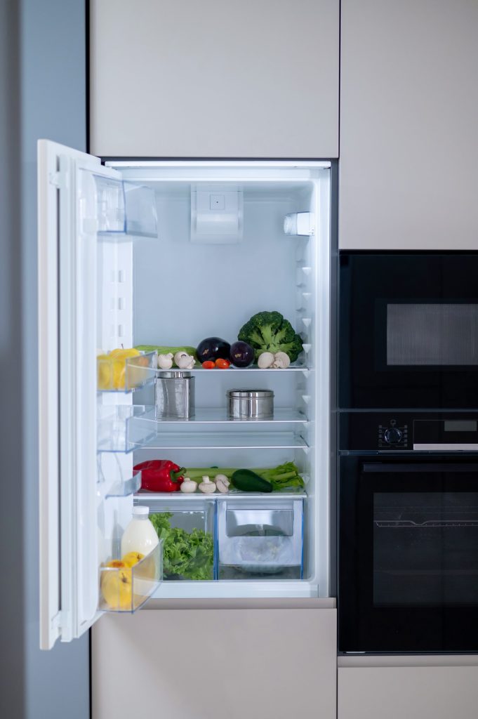 A built-in refrigerator standing open in a run of pale cabinetry, a microwave and an oven column at the right.