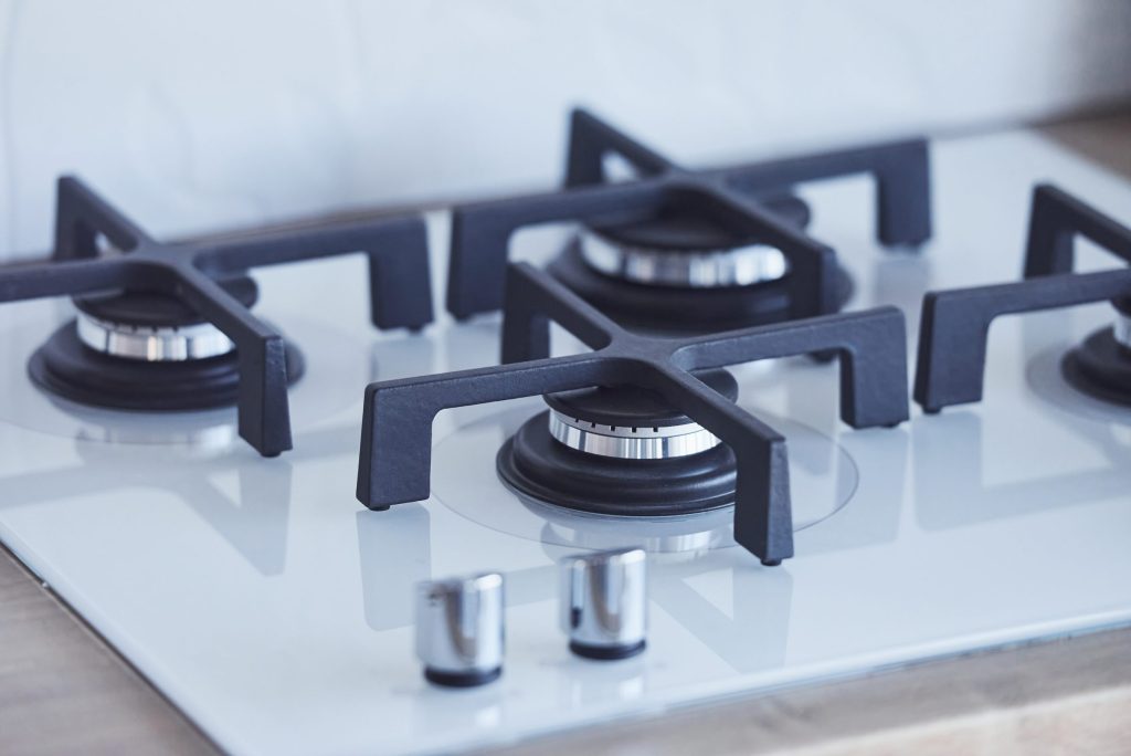 A gas cooktop seen from above — four burners with cast grates on white.