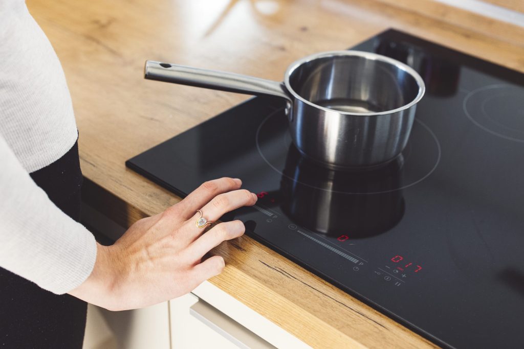A hand at the slider of an induction hob set in an oak worktop, a steel saucepan on the ring.