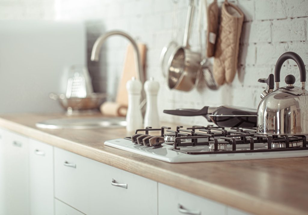 A kettle on a gas hob above a built-in oven in a cream kitchen.