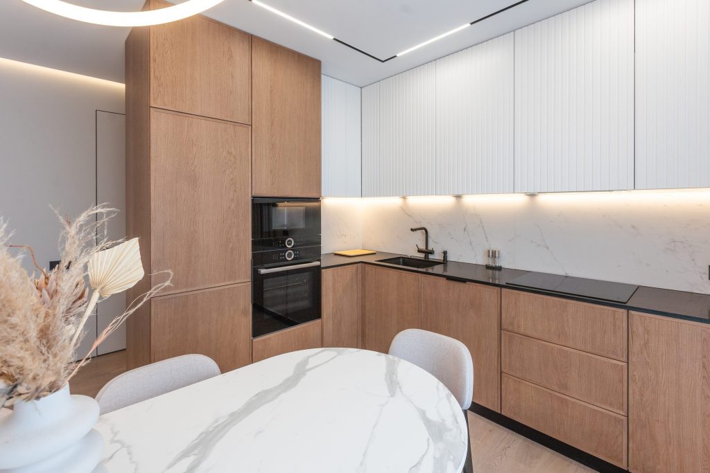 An oak and white kitchen run with a built-in oven beside a marble dining table.