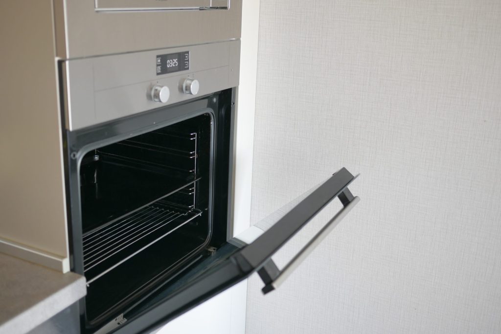 A stainless built-in oven with its door swung open against a plain pale wall, the empty racks and the drop-down door in view