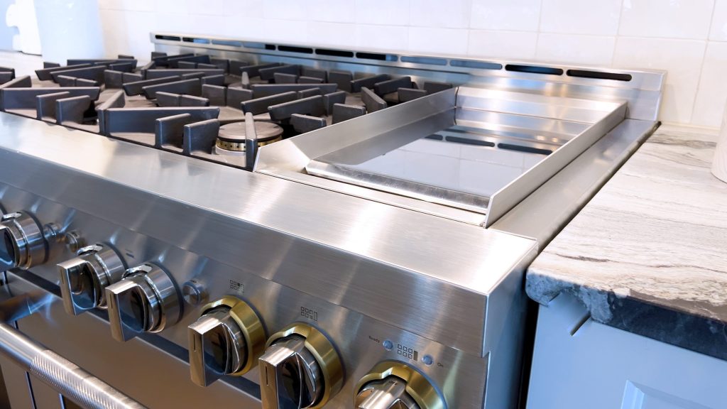 A stainless professional rangetop with a griddle plate, seen along the front edge.