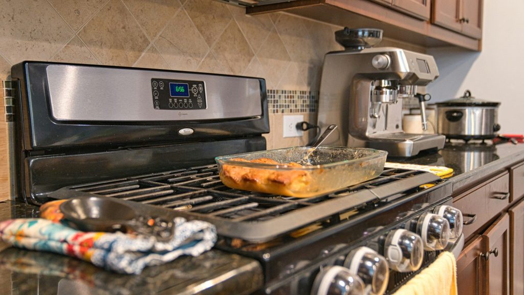 A stainless gas range in a kitchen of dark cabinets, a glass baking dish standing on the grates