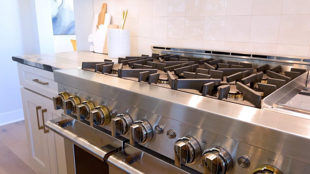 A wide professional gas range in a home kitchen, cast-iron grates and a row of metal control knobs