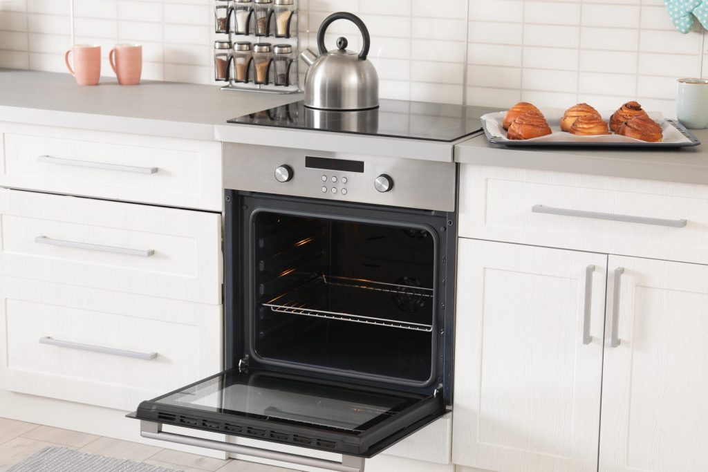 A stainless oven open with a tray cooling above it.