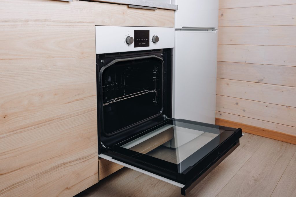 A white built-in oven open against a pale timber wall.