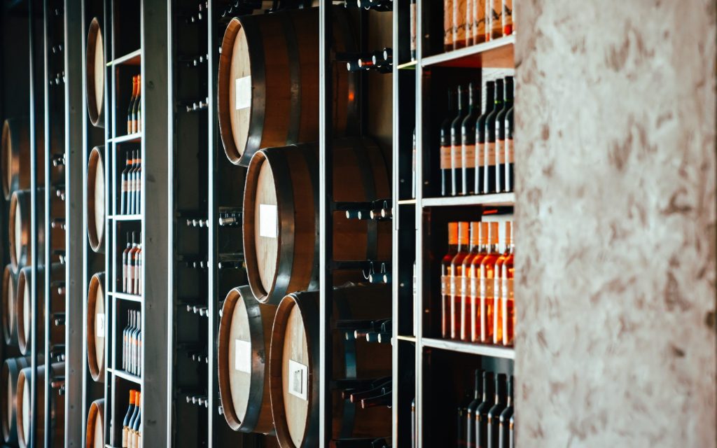 A lit wine room with barrels and bottles along the shelves.