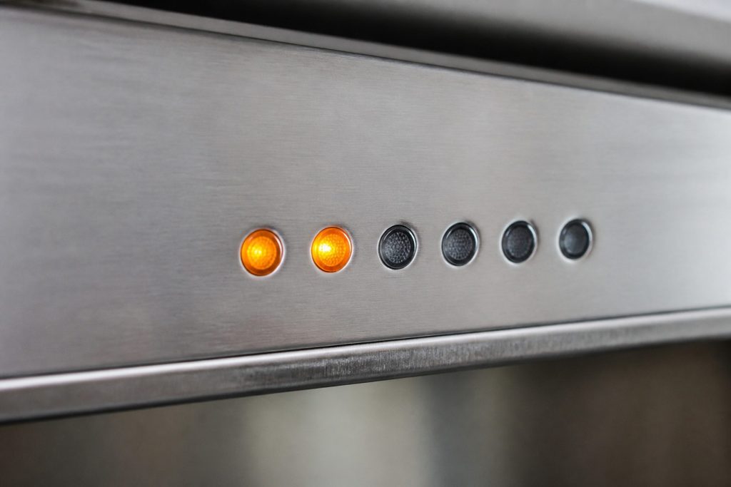 A close view of a row of small round indicator lamps on a brushed appliance fascia, two of them lit, no digits and no text anywhere on the strip, shallow focus, cool daylight.