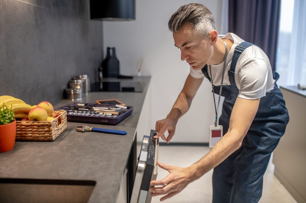A technician reading a cooktop control panel, socket set open on the counter.