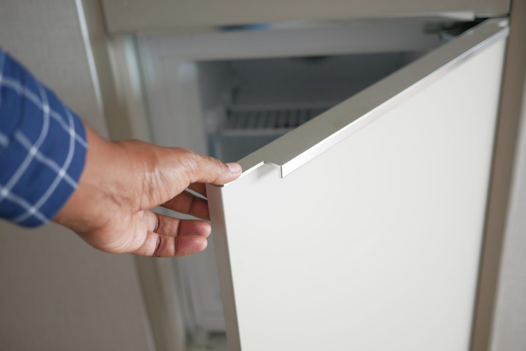 A hand on the edge of an open white refrigerator door, the seal and door edge in close view