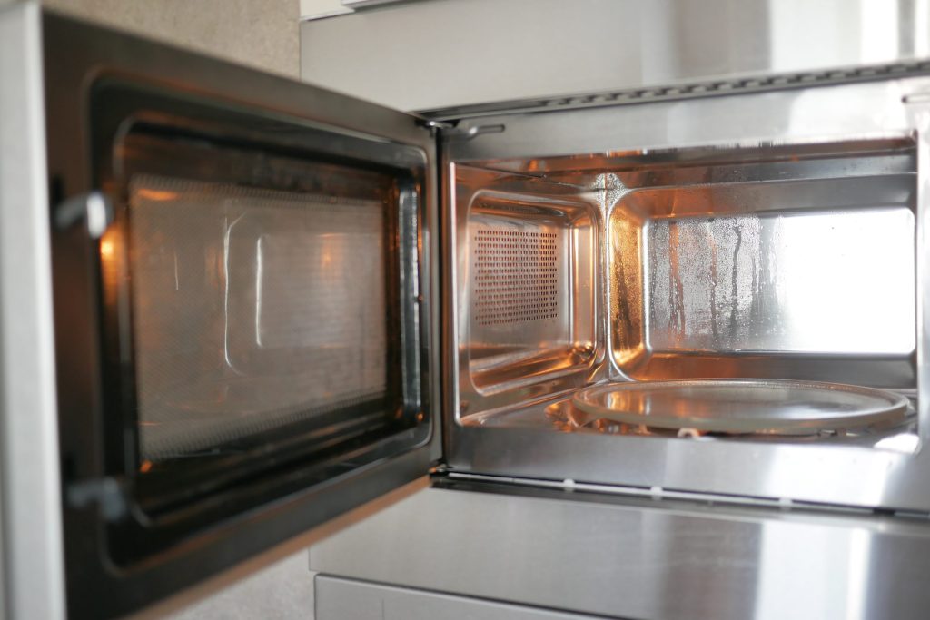 A microwave standing open, its stainless cavity and turntable clean and empty.