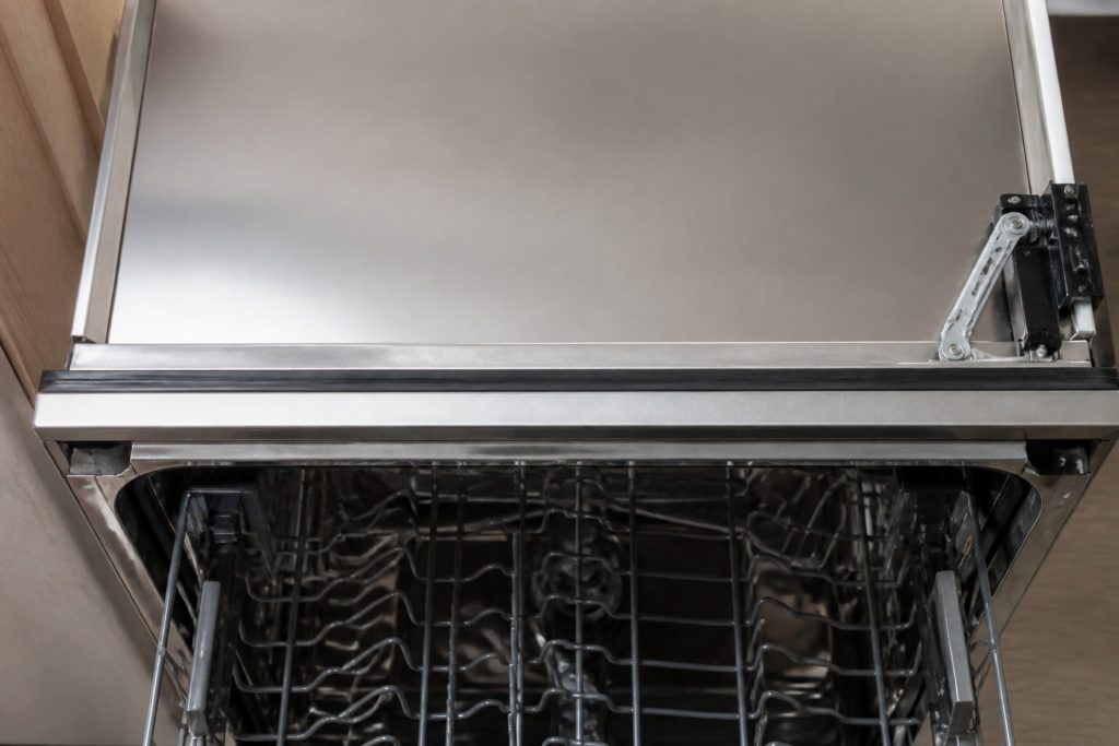The raised flat lid of an open dish drawer seen from above and close, the horizontal rubber seal running the full length of the tub rim in sharp focus, the small lid motor arm visible at one corner.