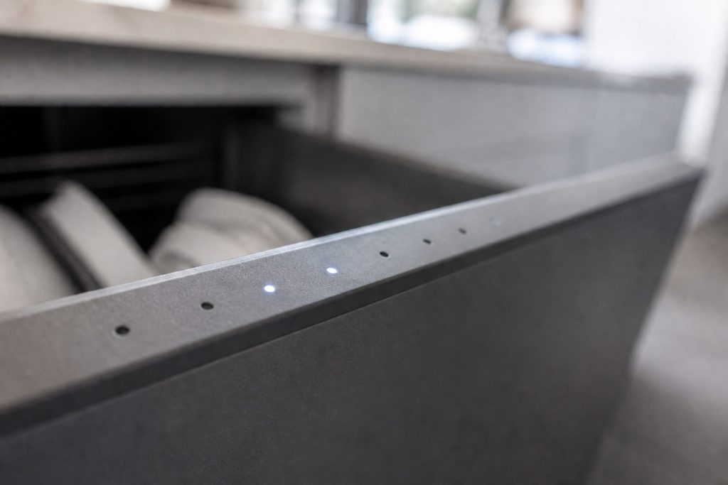 A close raking view along the top edge of a dish drawer front where a row of small round indicator lamps sits, two of them lit and no digits or text anywhere.